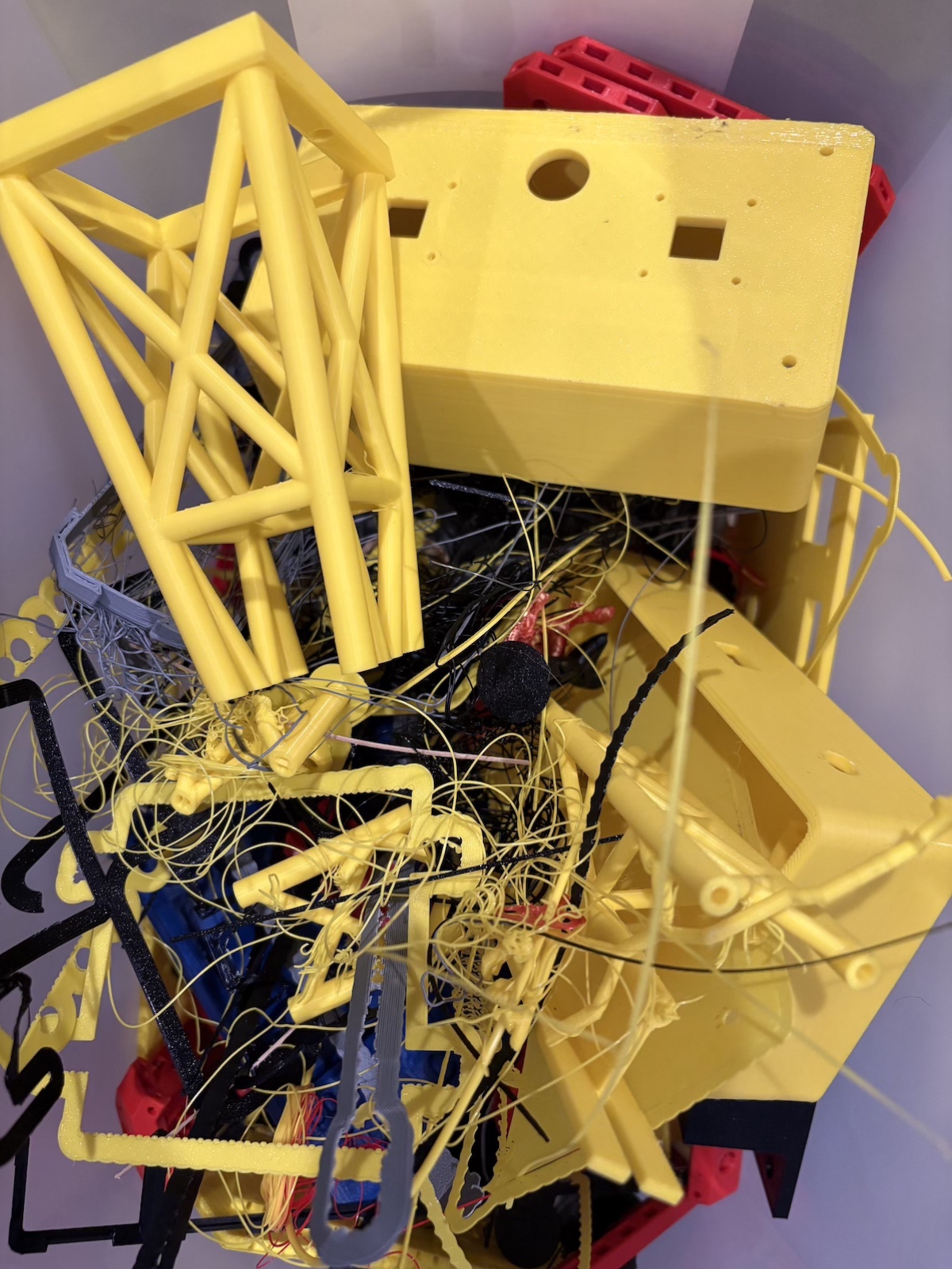 A pile of yellow, black, and gray failed prints in the shop corner.